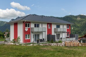 Ett tvåvåningshus med en röd och vit fasad, en täckt uteplats med utemöbler och en bergig bakgrund.
