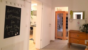 Un couloir avec une pancarte de bienvenue, une armoire en bois et un miroir décoré d’un motif en forme de cœur.