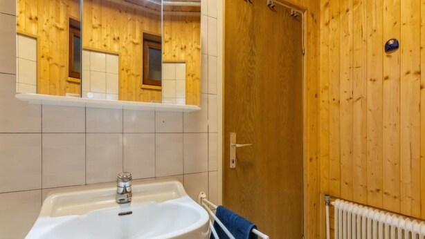A bathroom with a wooden wall, a white sink with a towel rack, and a door. - Pistenblick klein by Interhome (Sirnitz - Hochrindl)