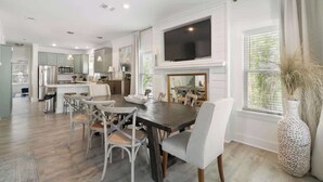 A modern kitchen with stainless steel appliances, a dining area with a large table and chairs, and a TV mounted above the fireplace.