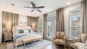 A bedroom with a large bed, a ceiling fan, a bench, a chair, and a small table.