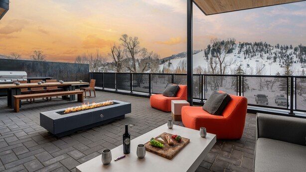 Une terrasse extérieure moderne, dotée d’un foyer, de sièges et offrant une vue sur un paysage enneigé.