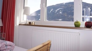 Ett sovrum med en säng, ett fönster med utsikt över bergen, en lampa och två äpplen på fönsterbrädan.
