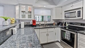 Cocina moderna con armarios blancos, encimeras de granito, microondas integrado y estufa de acero inoxidable.