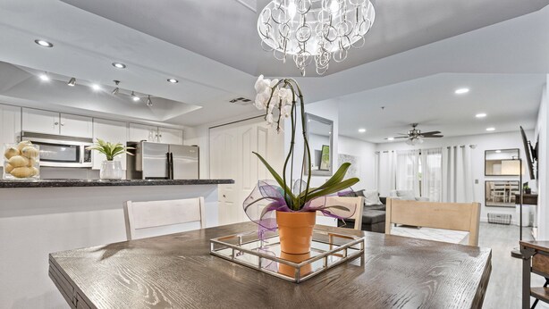 Una cocina moderna con armarios blancos, electrodomésticos de acero inoxidable y una mesa de comedor de madera con una orquídea en maceta.