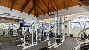 Un gimnasio con diverso equipo de ejercicio, ventanas amplias y techo de madera.