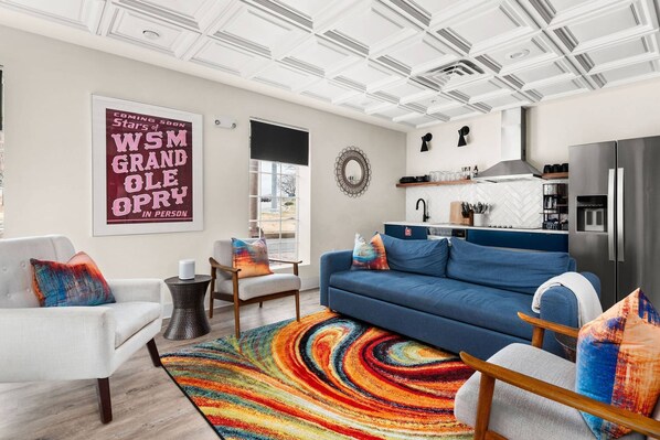 A modern living room with a blue sofa, white armchairs, and colorful rugs.