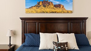 A bedroom with a wooden headboard, a bed with blue and white bedding, and a landscape painting on the wall. - 4-BR Home with a Private Heated Pool (Litchfield Park)