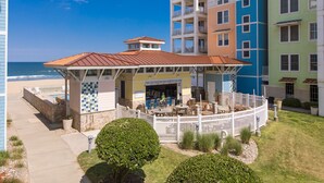 Um hotel na praia com varanda coberta, área de estar externa e vista para o oceano.