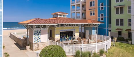 A beachfront hotel with a covered patio, outdoor seating, and a view of the ocean.