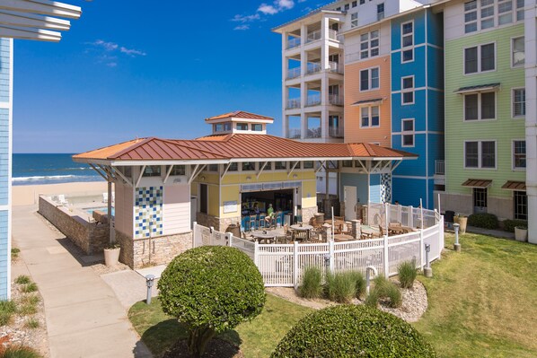 A beachfront hotel with a covered patio, outdoor seating, and a view of the ocean.
