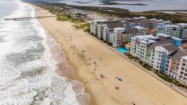 Um hotel à beira-mar com vários edifícios, uma praia arenosa e um cais que se estende para a água.
