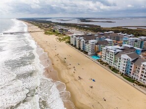 A beachside hotel with multiple buildings, a sandy beach, and a pier extending into the water.