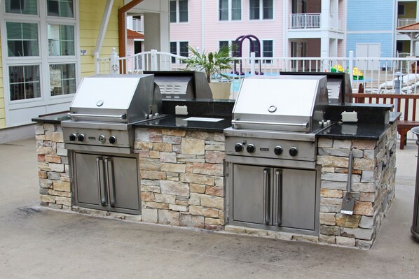An outdoor kitchen with two gas grills and a built-in oven, surrounded by stone walls.