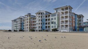 Hotel à beira-mar com várias varandas e uma praia arenosa em primeiro plano.