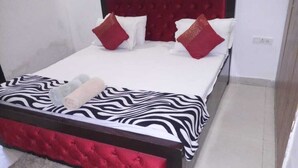A bed with a zebra-patterned bedspread, red and white pillows, and a red upholstered headboard. - Beautiful 3BHK Apmt at Iconic Location Chattarpur (Sat Bari)