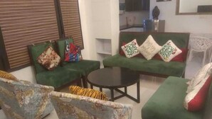 Un salon avec un canapé vert, une table basse ronde et des fauteuils à motifs.