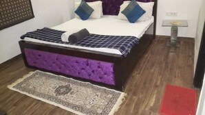 Un lit avec une tête de lit rembourrée de tissu violet, une literie blanche et des oreillers bleus et blancs.