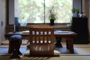 A traditional Japanese room with tatami flooring, a low wooden table, a cushioned bench, and a window with a view of greenery.