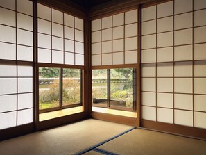 A traditional Japanese room with tatami flooring, shoji screens, and a view of a garden.
