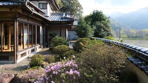 A traditional Japanese building with a wooden exterior and tiled roof, surrounded by lush greenery and a view of a river and mountains. - Shimanto Riverside Hideaway (Shimanto)