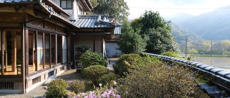 A traditional Japanese building with a wooden exterior and tiled roof, surrounded by lush greenery and a view of a river and mountains.