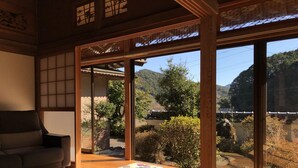 A traditional Japanese-style room with tatami flooring, a low wooden table, and cushions. Large windows offer a view of a mountainous landscape. - Shimanto Riverside Hideaway (Shimanto)