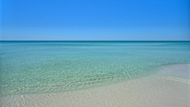 A clear view of a beach with shallow, clear water and a sandy shore.
