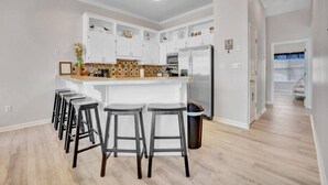 A modern kitchen with white cabinets, a central island with stools, and a refrigerator.