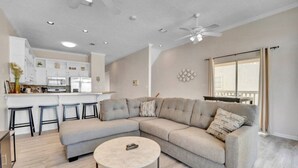 A modern living room with a sectional sofa, a round coffee table, and a kitchen area with bar stools.