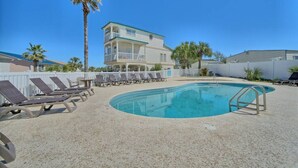 A swimming pool with lounge chairs, a palm tree, and a two-story building in the background.