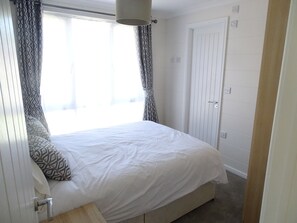A bedroom with a bed, curtains, a door, and a light fixture. - Luxury 2 Bedroom Lodge (sleeps 5) (North Runcton)