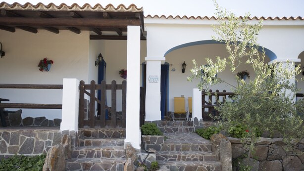 A stone staircase leading to a white building with a wooden fence and a blue door. - Country house Comfort apartment with parking place (Sardegna)