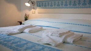 A neatly made bed with white and blue linens, a wall clock, and a decorative wall pattern. - Country house Comfort apartment with parking place (Sardegna)