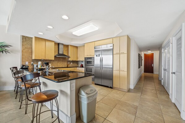 A modern kitchen with a central island, bar stools, stainless steel appliances, and wooden cabinetry.