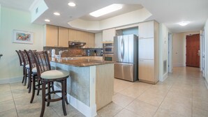 A modern kitchen with a central island, stainless steel appliances, and a dining area with bar stools. - Cozy Three Bedroom with Spectacular Gulf Views! Complimentary Boat Slip! (Orange Beach)