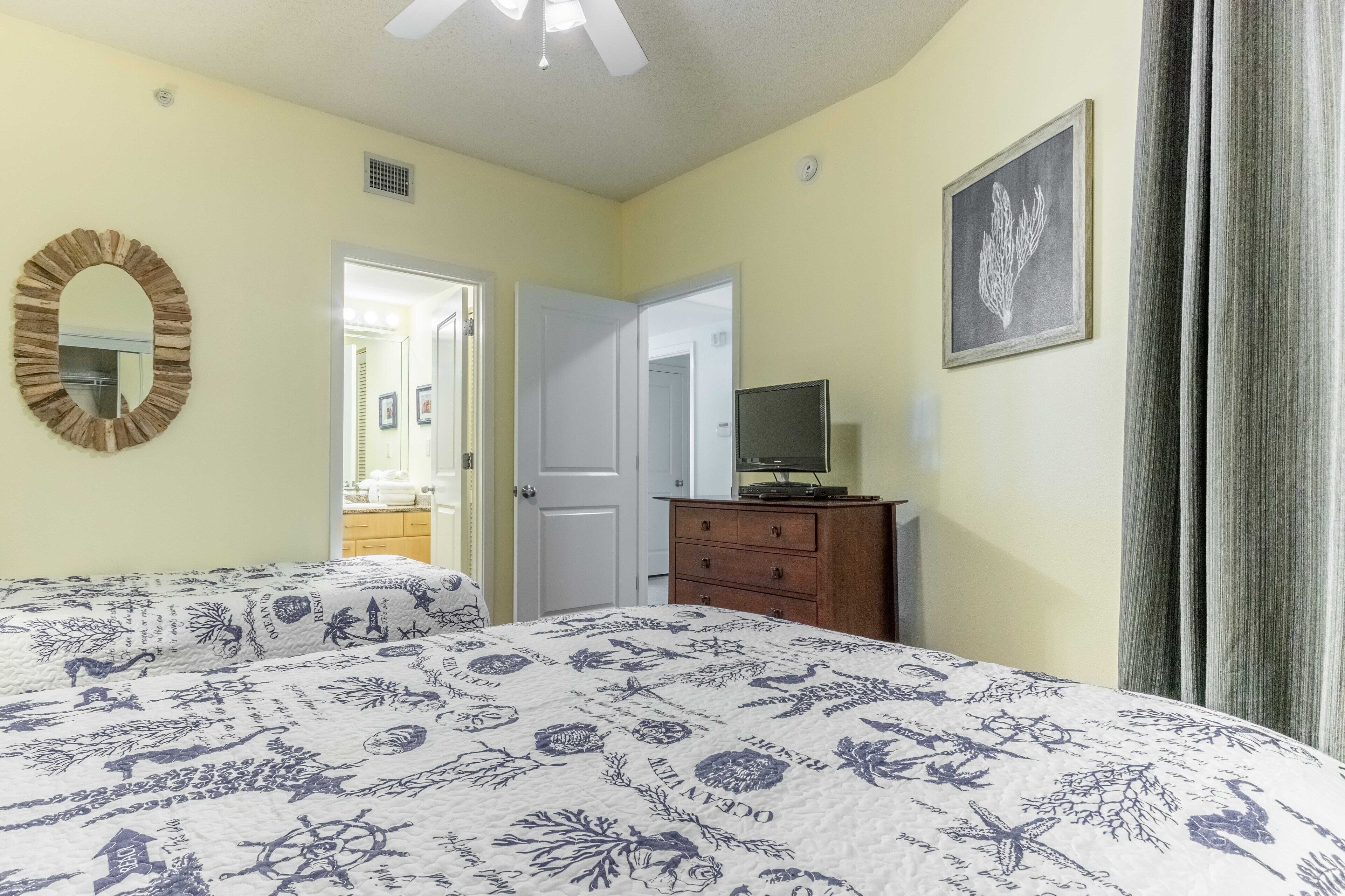 Une chambre à coucher comprenant un lit, une commode, un téléviseur et une porte donnant sur une autre pièce.