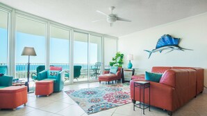 A spacious living area with a large sliding glass door leading to a balcony, a ceiling fan, and a decorative fish mural on the wall. - Cozy Three Bedroom with Spectacular Gulf Views! Complimentary Boat Slip! (Orange Beach)