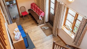 A cozy room with a wooden bench, a small table with a tissue box and a toy bus, a pair of slippers on the floor, and a window with curtains. - 3-bed Barn Eco-lodge on the Tarka Trail (Torrington)