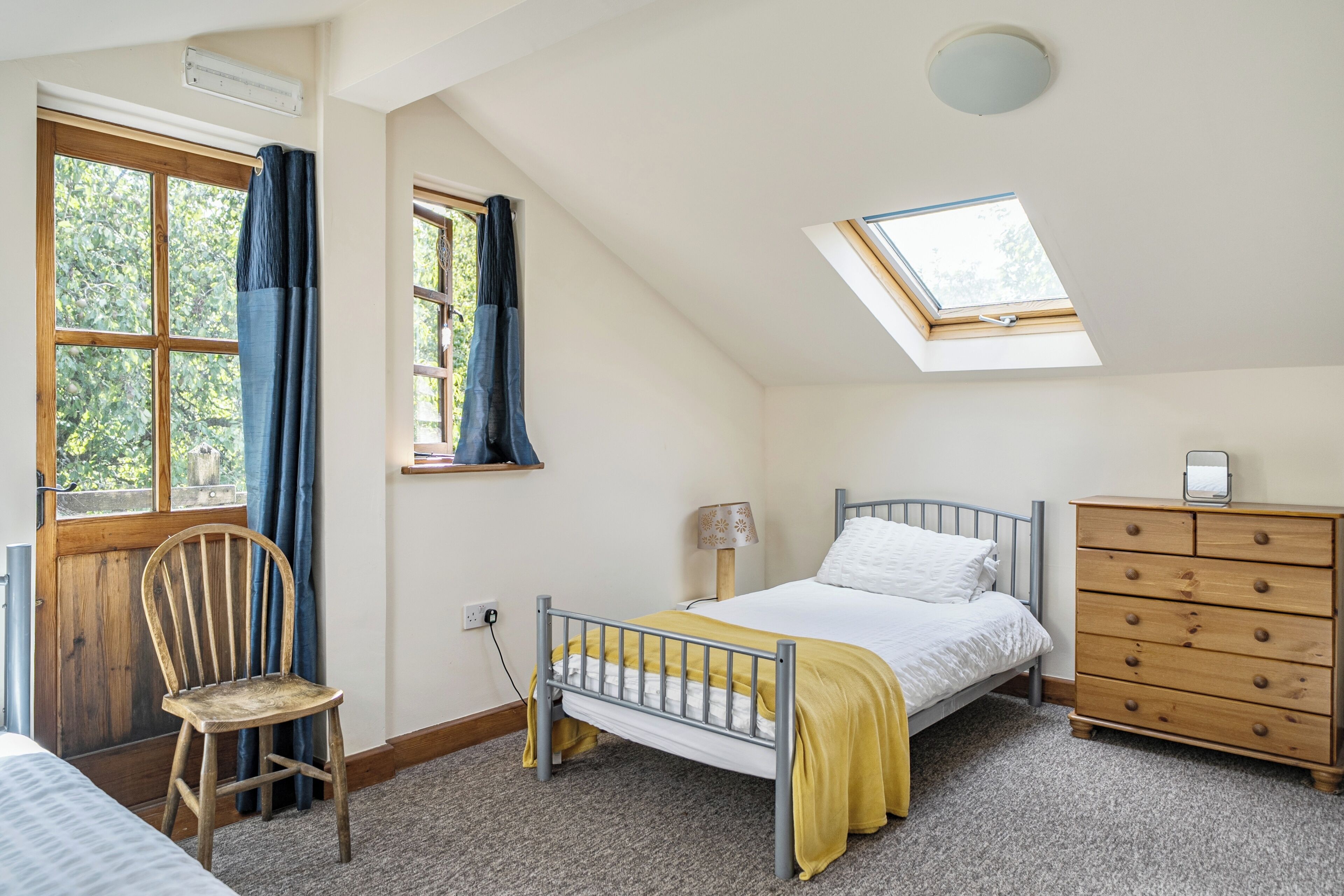 Ein Schlafzimmer mit Bett, Kommode, Stuhl, Fenster und Dachfenster.