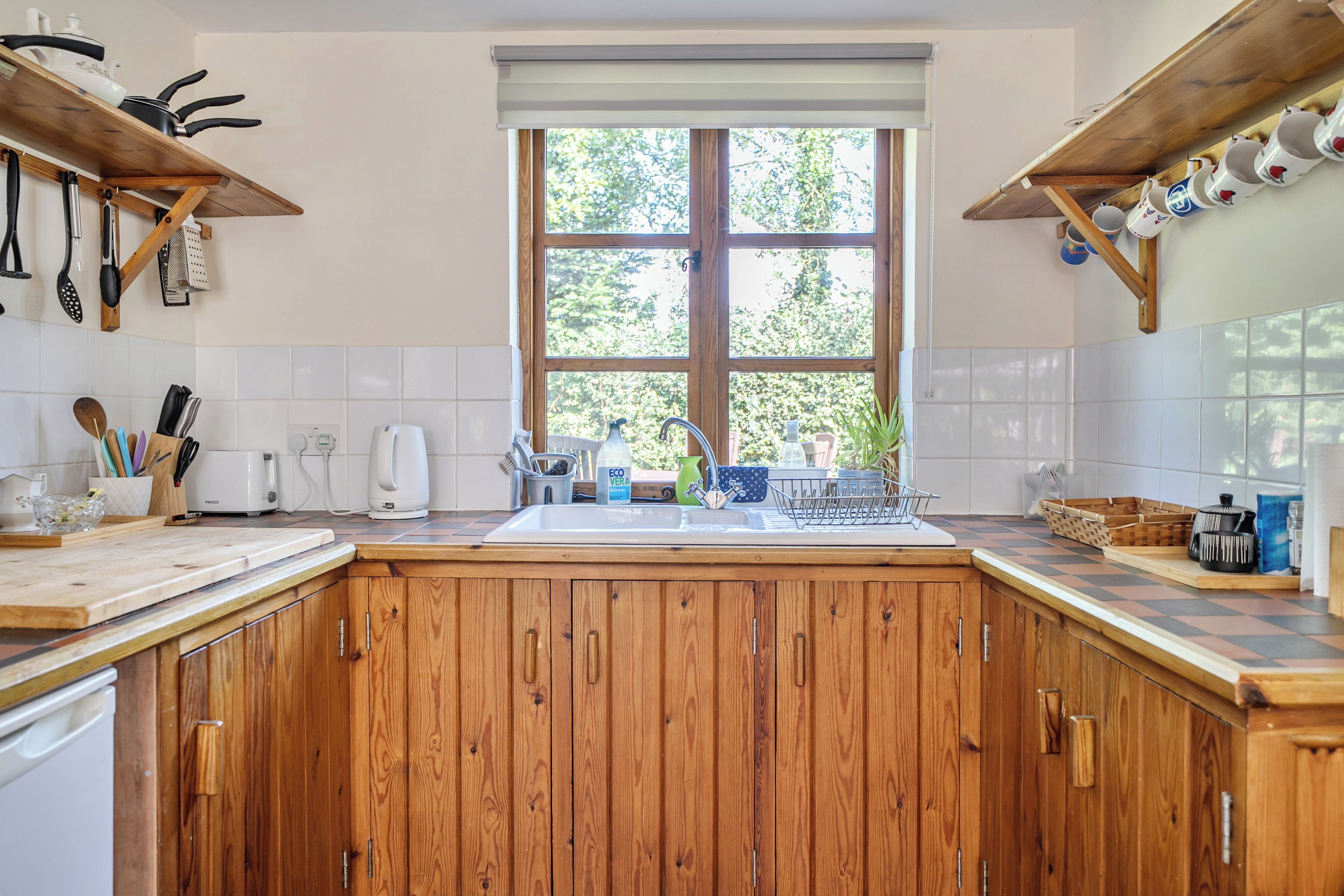 A kitchen with wooden cabinets, a window, and various kitchen utensils.