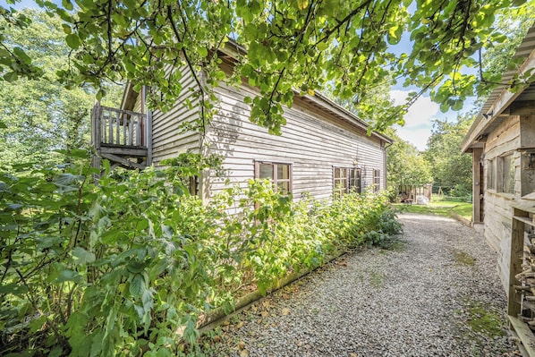 A wooden house with a gravel driveway and a wooden fence. - 3-bed Barn Eco-lodge on the Tarka Trail (Torrington)