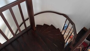 Un escalier en colimaçon en bois, doté d’une rampe et d’un luminaire fixé au mur.