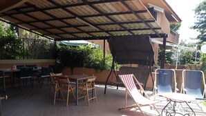Une terrasse extérieure dotée d’un espace salon couvert, de tables et de chaises.