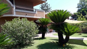 Un immeuble résidentiel doté d’un balcon, entouré de pelouses bien entretenues et de palmiers.