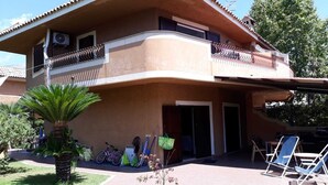 Une maison à deux étages avec un balcon, un patio aménagé avec des chaises et un vélo garé à l’extérieur.