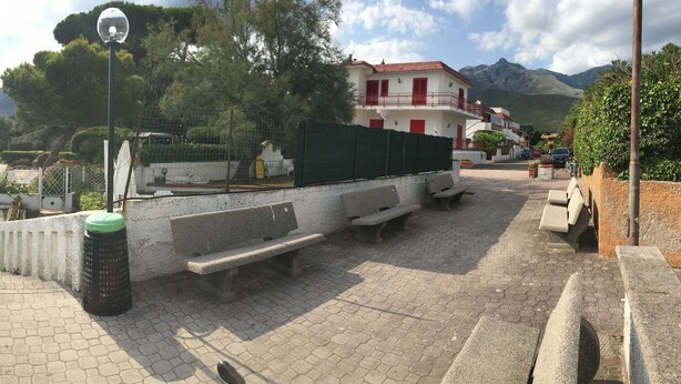 Une plage avec une promenade dallée, des parasols et un bâtiment doté d’un toit rouge.
