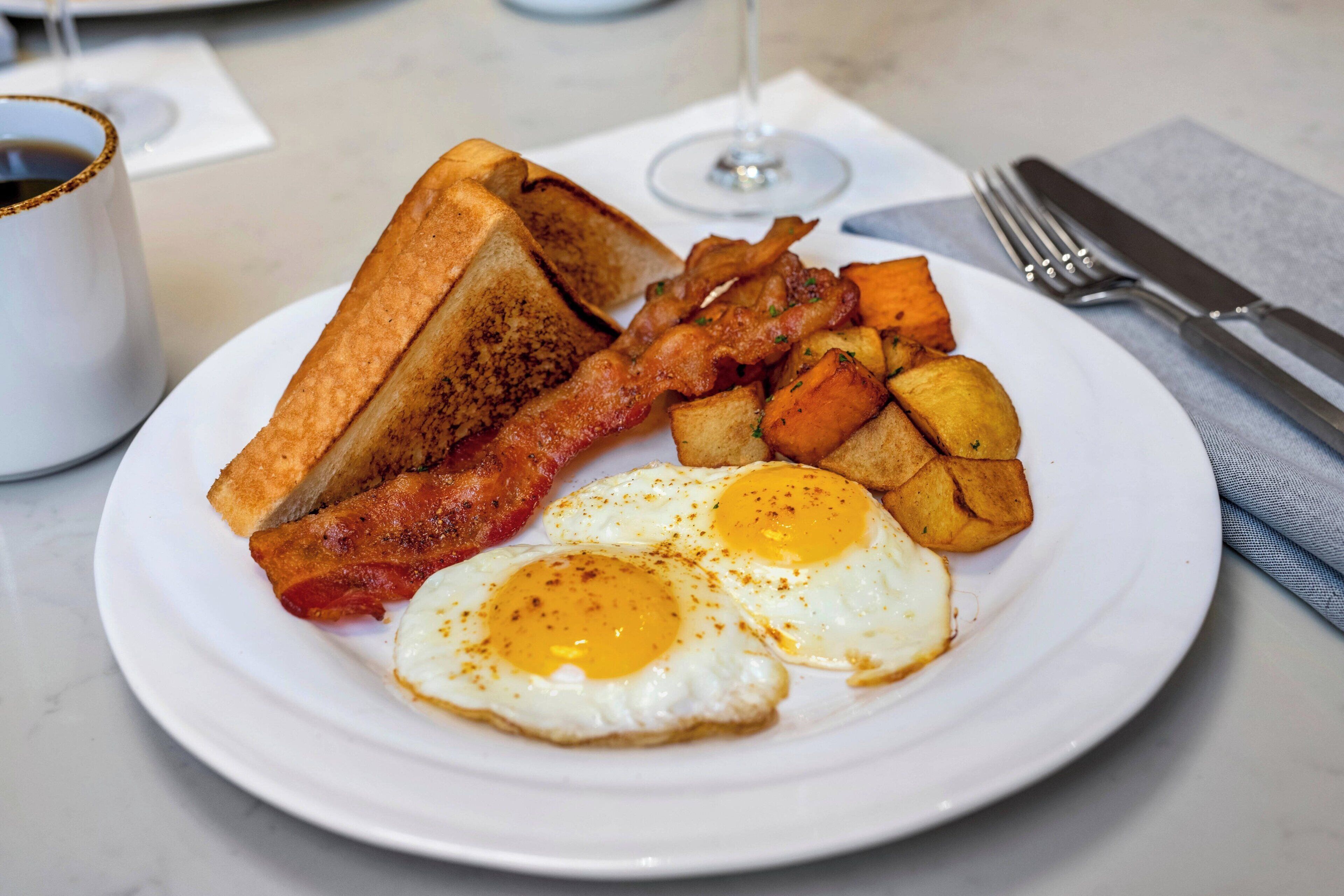A plate with toast, bacon, fried eggs, and potatoes.