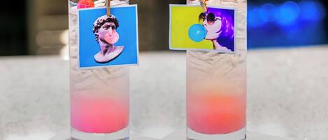 Two cocktails with colorful layers and small pictures on the rim, placed on a white surface.