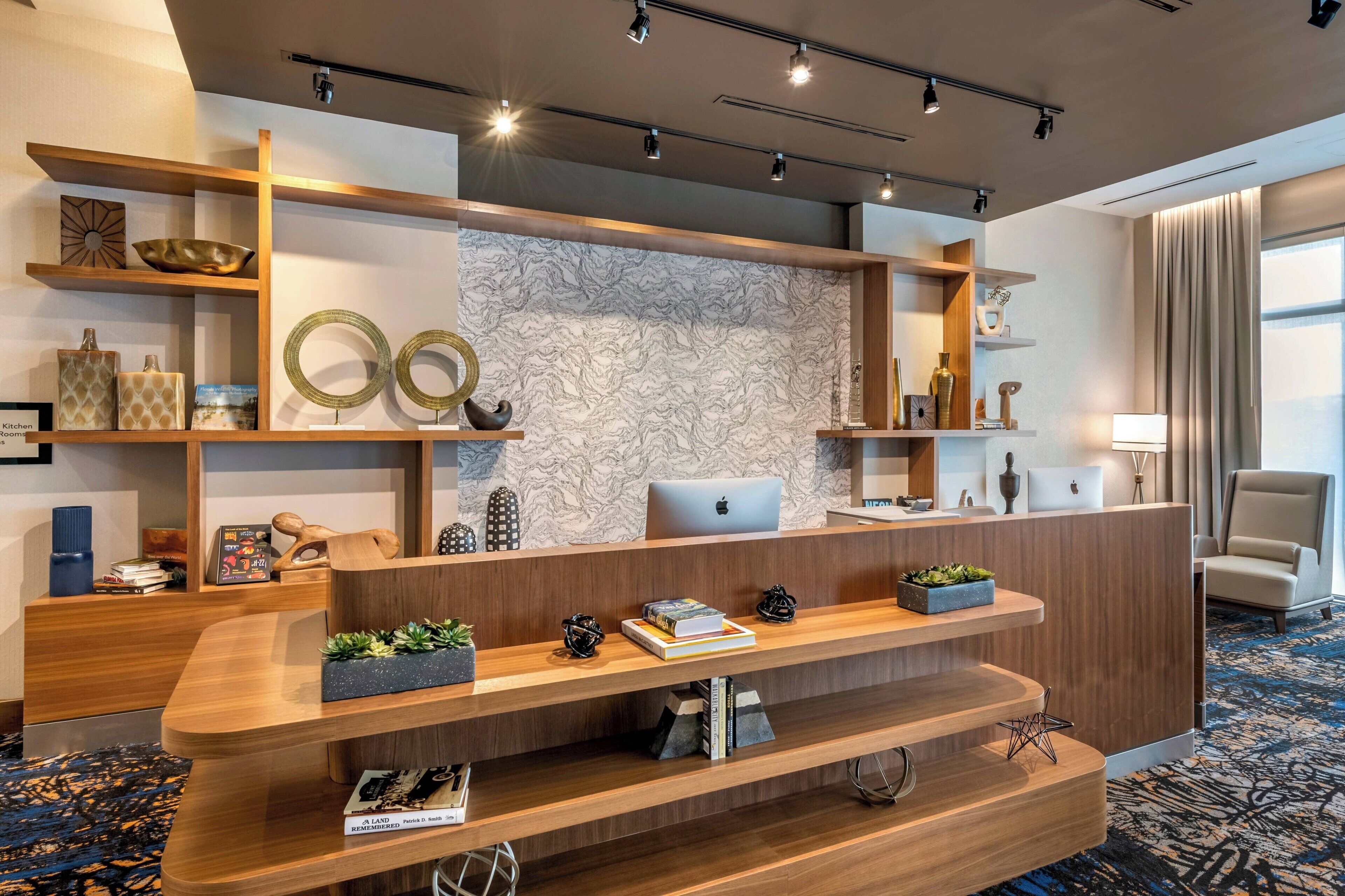 Un mostrador de recepción moderno con una computadora portátil, rodeado de estanterías con objetos decorativos y una pared con diseño de mármol.